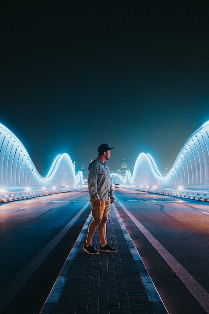 A man stands on a modern illuminated bridge at night, showcasing city lights.