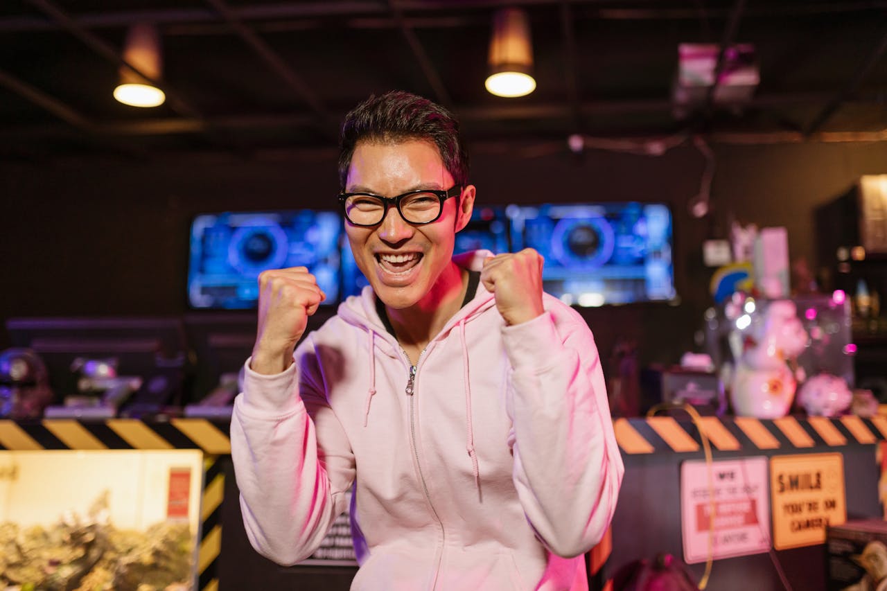 Excited gamer in hoodie celebrates a win indoors with a cheerful smile.
