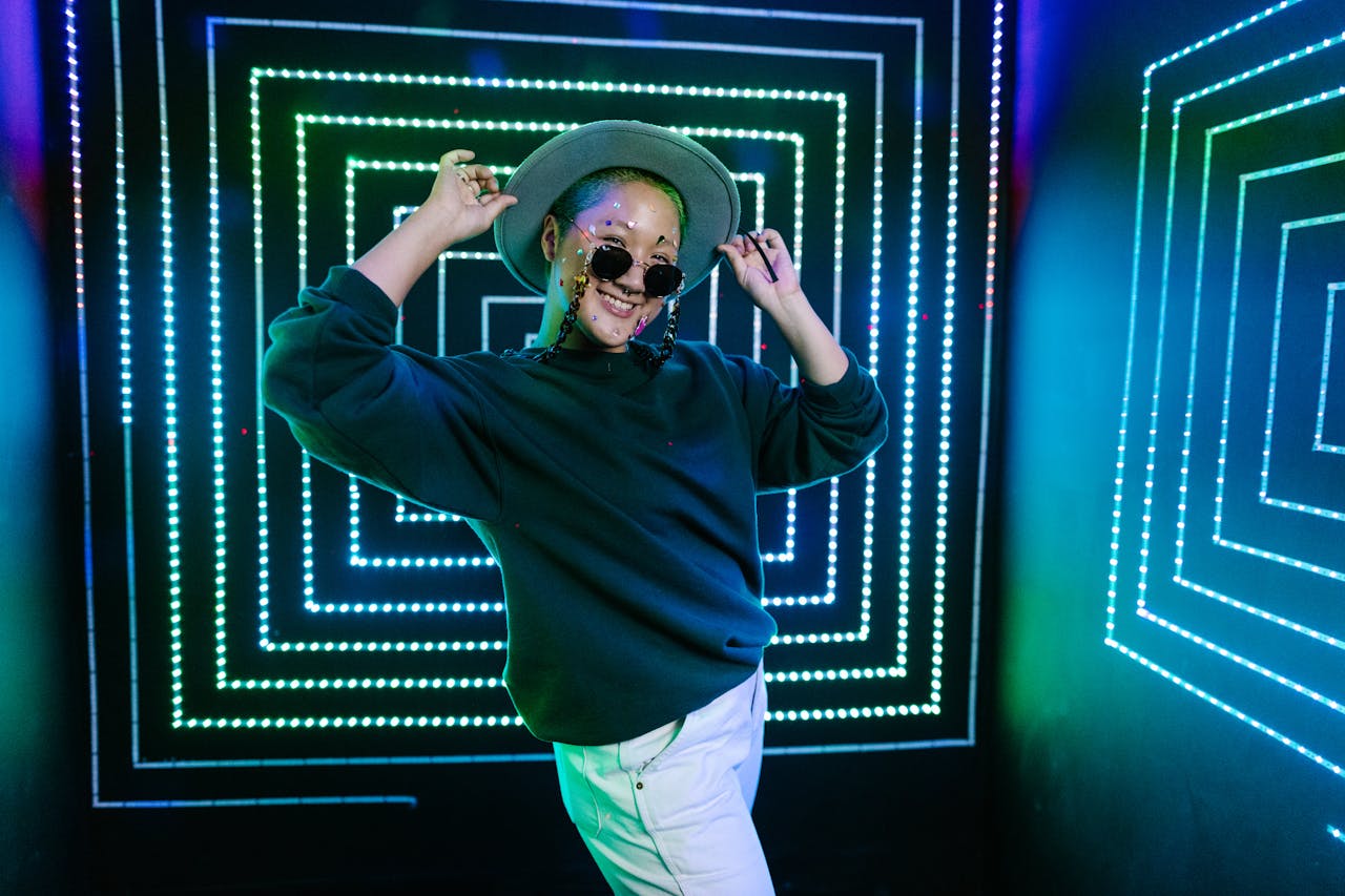 A fashionable woman poses confidently in a vibrant room with neon lights and geometric patterns.