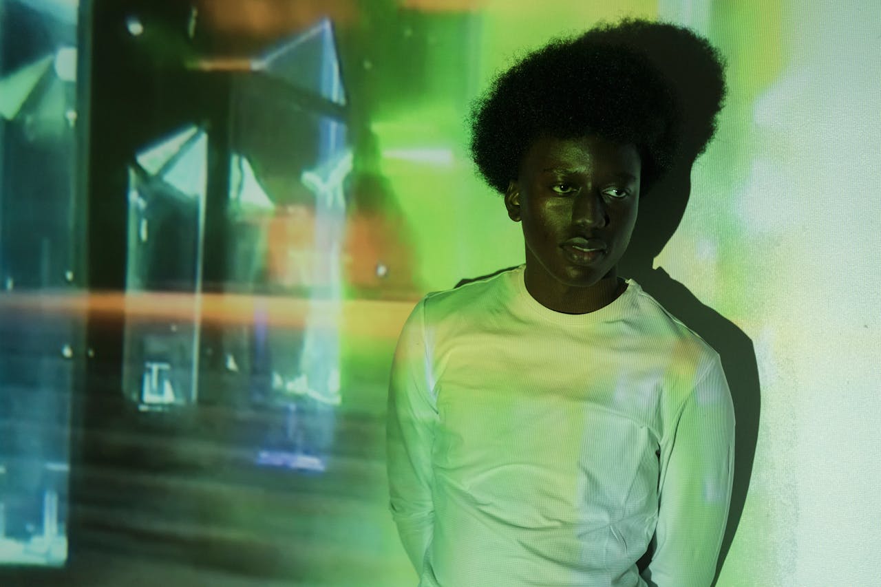 A black man with afro hair stands against projections in a studio shoot.